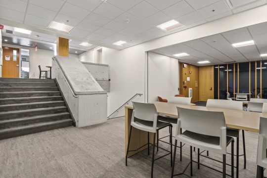 a common area with a set of stairs going up and another going down, with a table and chairs on the main level.