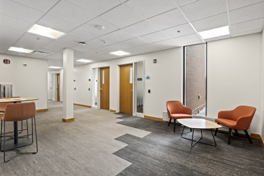a common area with tables and chairs that leads to a hallway with offices.