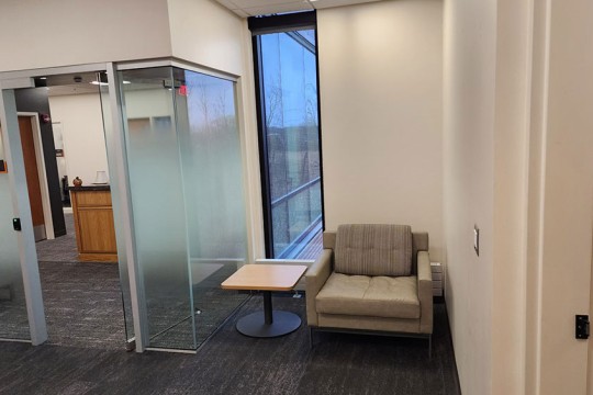 a corner next to a glass office, with a chair and end table.