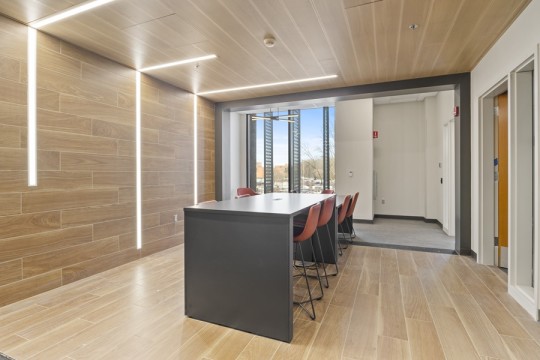 a modern meeting space with wood tile on the floor and wall, and a high topped table in the center.