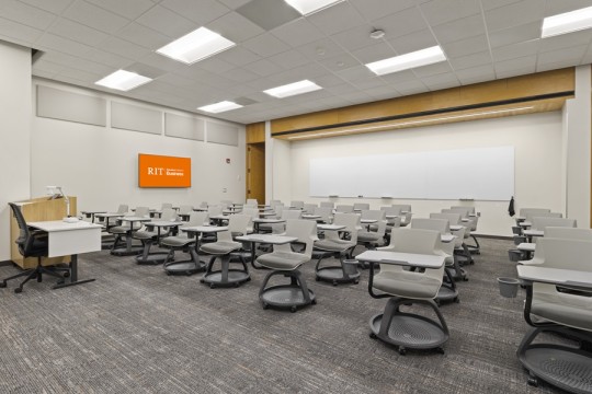 a large classroom with desks and chairs and a large whiteboard in the back.
