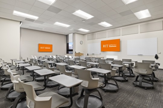a large classroom with individual desks and chairs, and two large whiteboards and T Vs on the wall.
