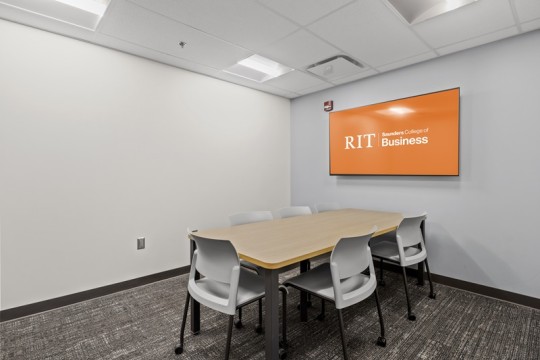 a meeting room with a table and five chairs, and a large T V on the wall.