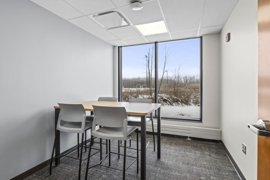 a meeting room with a table and four chairs, and a large window.