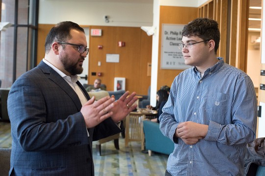 Two men having a conversation in the lobby of Lowenthal Hall.