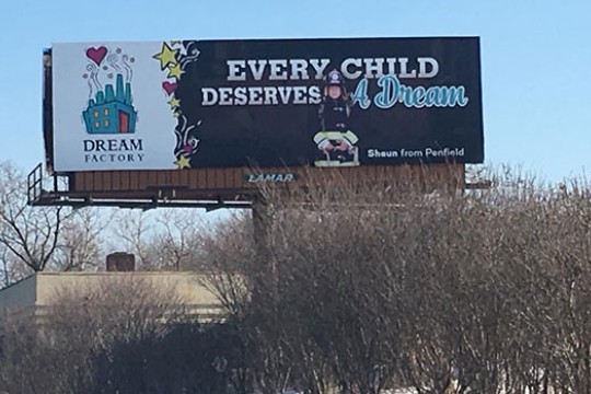 A photo of the billboard designed by the advertising and promotion management class. It reads, "Every Child Deserves A Dream" in large text on the right, and on the left there is a illustrated photo of a small factory with the words "Dream Factory" written below.