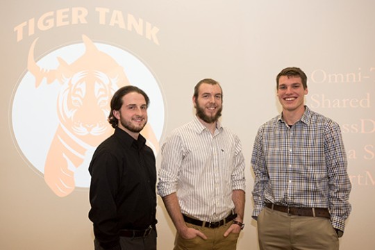 Three people in button down shirts standing in front of Tiger Tank logo.