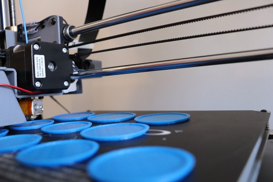 A 3D printer at work, printing 10 blue, flat, circular objects.