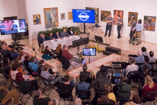 Overhead view of sitting crowd listening to presenters.