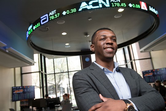 Student poses below stock ticker sign.