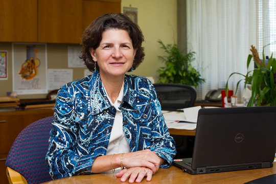 Woman wearing blue patterned blazer sits next to laptop.
