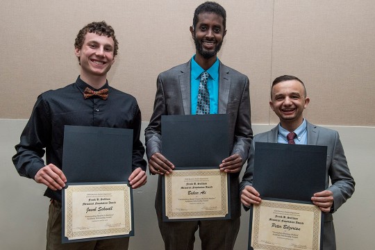 Jacob Schwall, Bakar Ali and Peter Bilzerian stand holding awards.