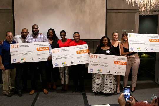 Nine people stand holding four giant novelty checks for $10,000 each.