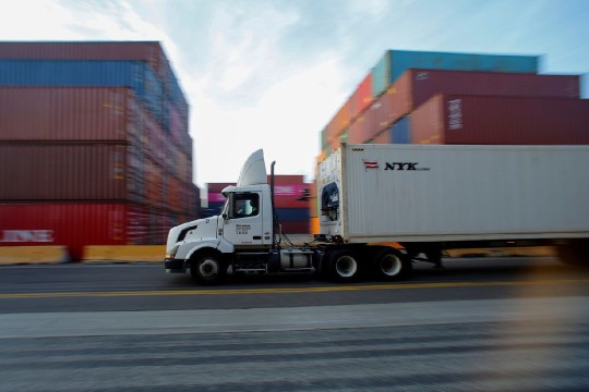 A semi truck carries its cargo through a shipment yard. 
