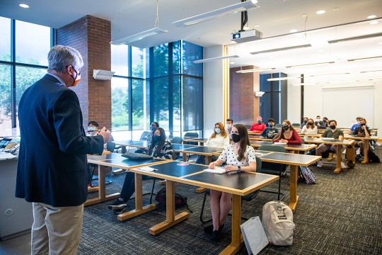 professor standing in front of classroom with students sitting socially distanced.