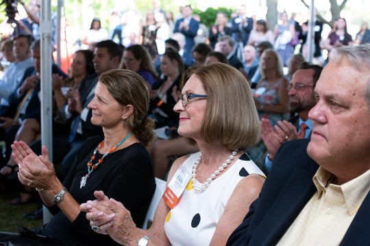 audience seated outdoors under a tent applauding.