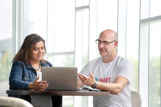 two students sit as a desk in a brightly lit social space.