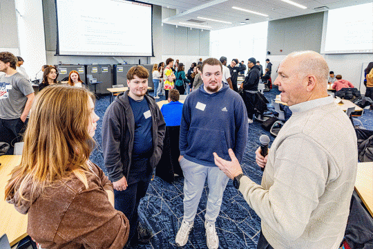 A group of four people stand speaking in a business classroom.