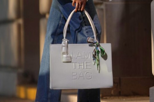 womens legs dressed in jeans are shown behind a white leather bag that says 'I am the bag' in a city setting.
