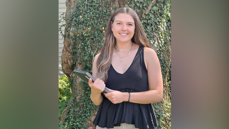 Edie Wilson smiling with a computer in hand in front of a tree
