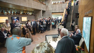 a crowd packs an atrium as a man speaks at a podium.