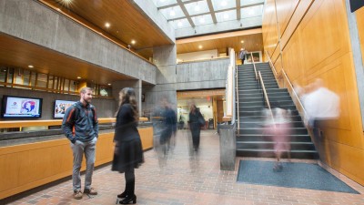 student and professor talk in an atrium as other people walk by, and their motion causes their images to be blurry.