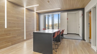 a modern meeting space with wood tile on the floor and wall, and a high topped table in the center.