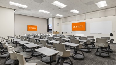 a large classroom with individual desks and chairs, and two large whiteboards and T Vs on the wall.