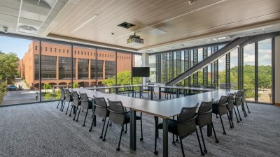 a large meeting space surrounded by floor to ceiling windows, and a large rectangular table with chairs in the middle.