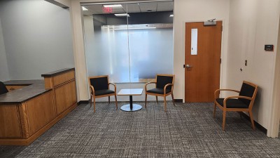 a reception area with an empty desk and three chairs.