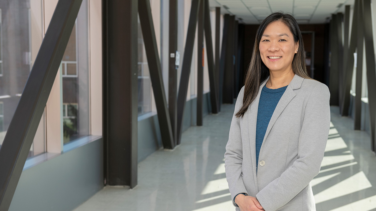 Faculty member standing in a hallway, next to large windows.