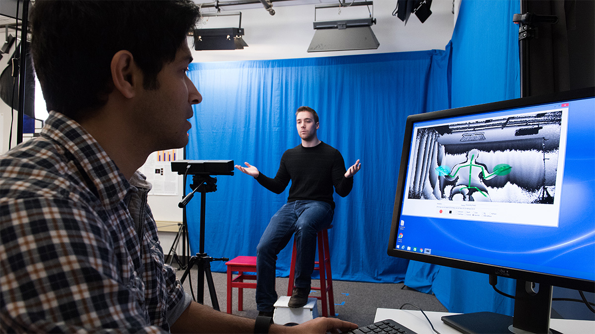 Two students in a lab, using body-recognition software to see students movements on a screen.