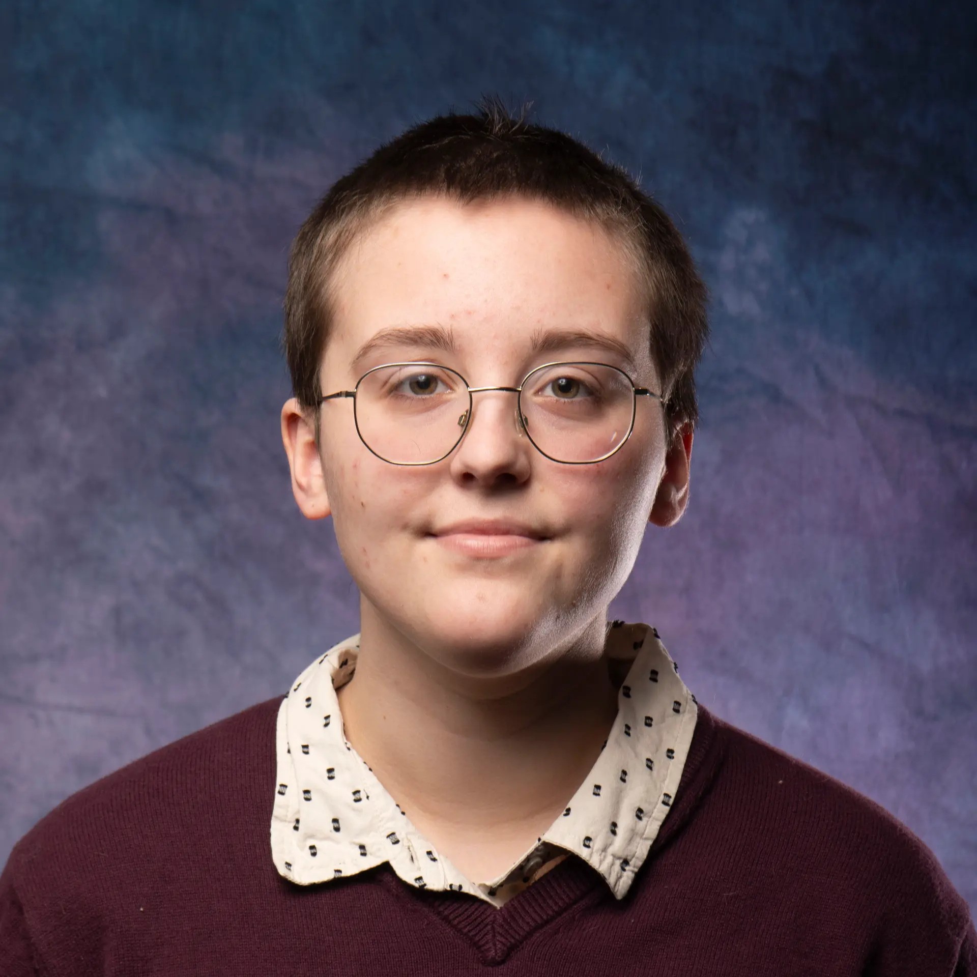 Chris is a white male with short brown hair with circular glasses and a maroon sweater