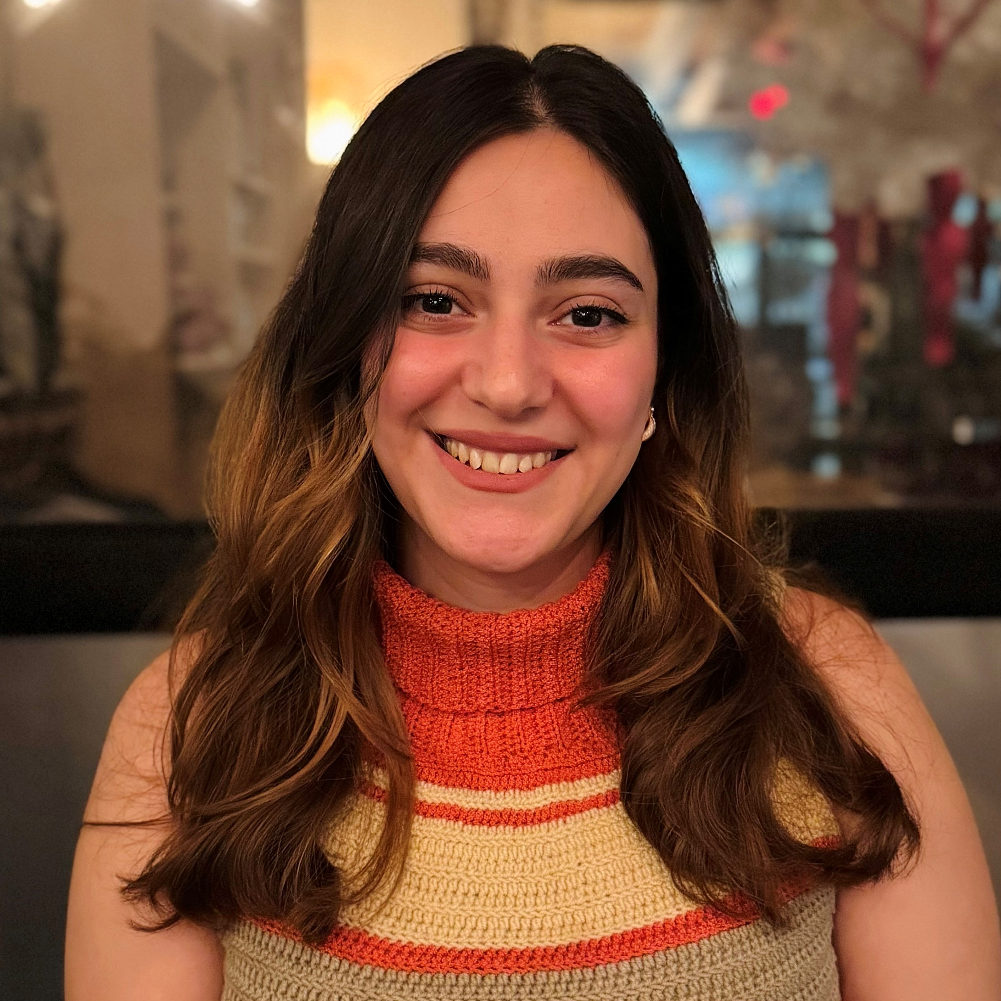 The photo shows Laleh, a woman with long brown hair, wearing an orange and while turtleneck top, facing the camera smiling. 