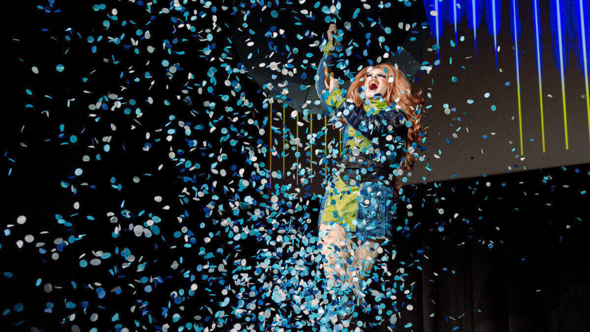 Pattie Gonia popping confetti on the stage during their keynote speaker event 