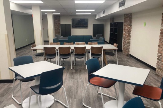 a lounge space with a long table with chairs and two smaller tables with chairs.