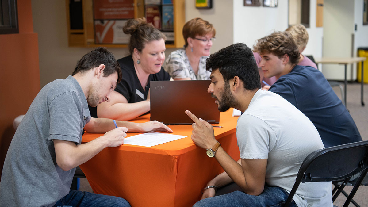 Two students work together at a table with staff members during an advising session.