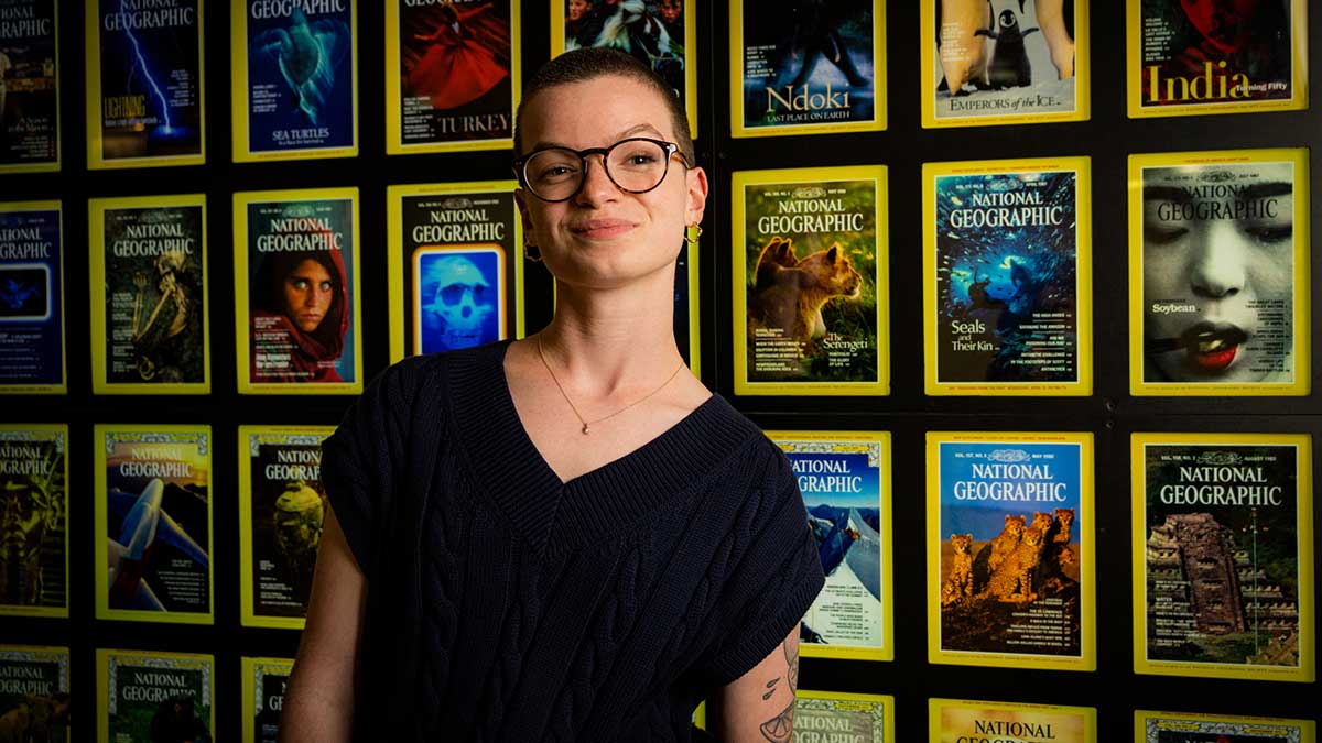 a woman smiles in front of a display of National Geographic magazines.