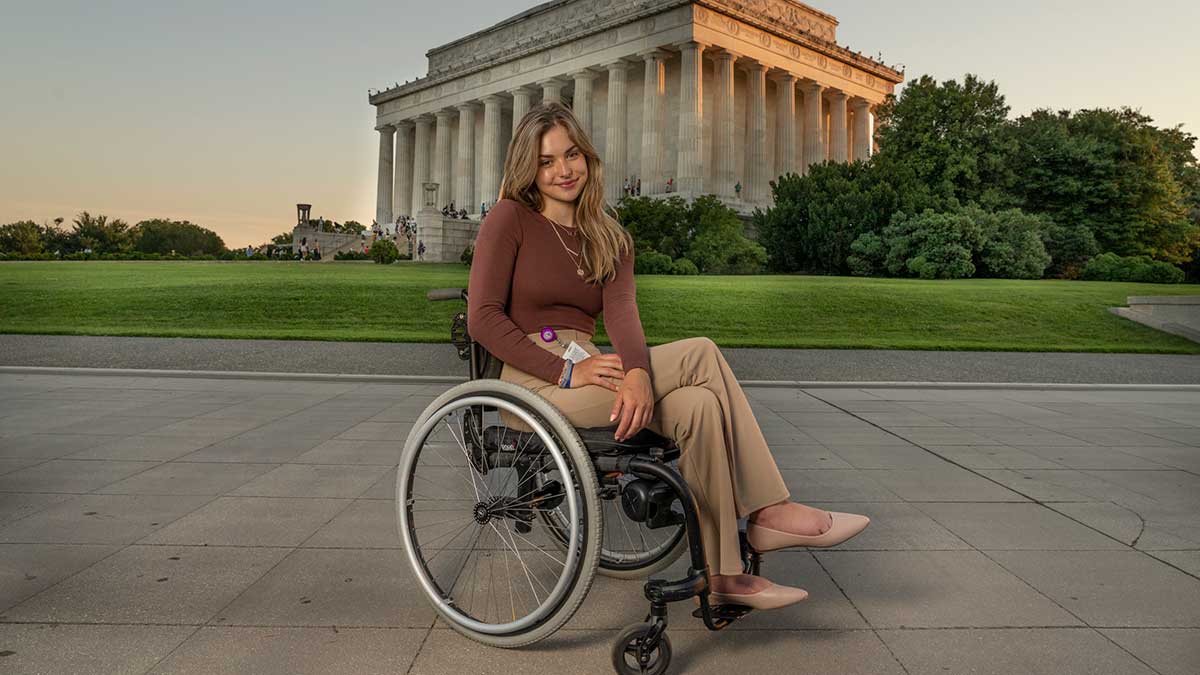 A woman in a wheelchair poses outdoors in front of the Lincoln Memorial at sunset.