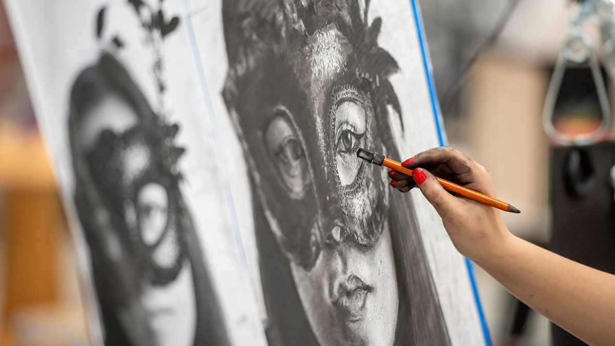 An artist’s hand draws a detailed charcoal portrait of a woman wearing a mask.