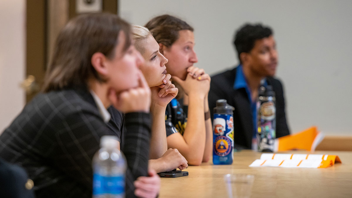Four people sit at a table listening attentively during a presentation.