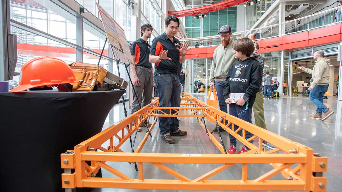 Two people demonstrate a steel bridge brace during the Imagine RIT festival.