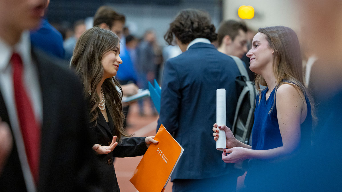 A recruiter gestures while talking with a student at a busy Spring Career Fair event.
