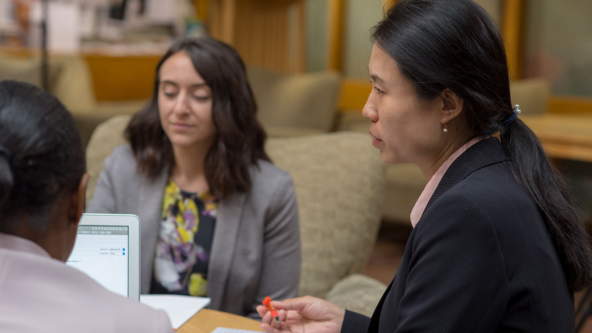 Two women in business attire have a focused conversation while seated with a laptop.