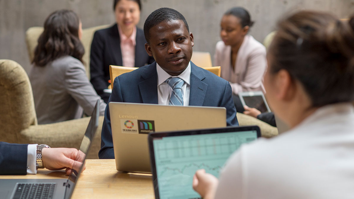 A man in a suit listens intently during a group discussion with laptops open.