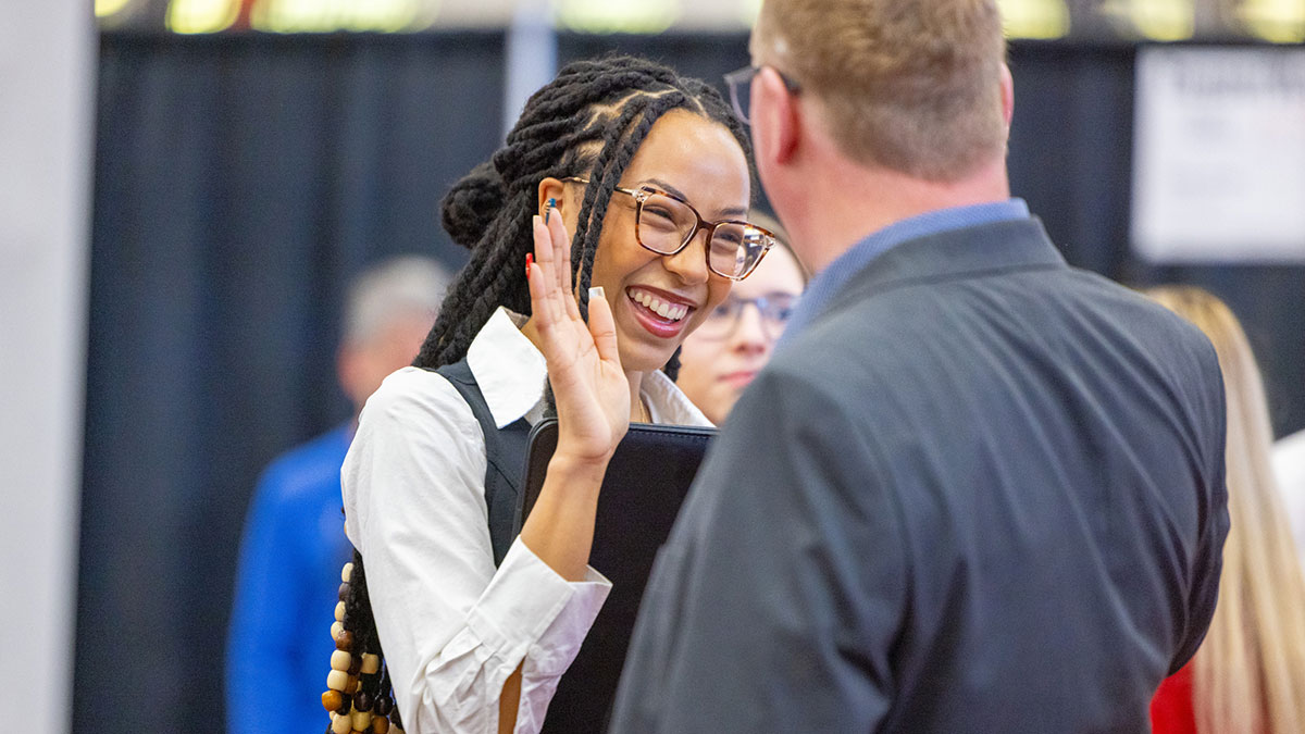 a student high-fiving a recruiter at a job fair.