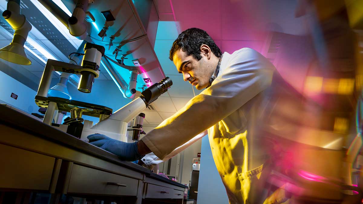 A researcher in a lab coat works with a microscope and specialized instruments.