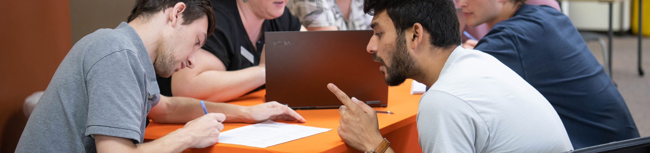 Several people sitting at a table in pairs, talking to each other.