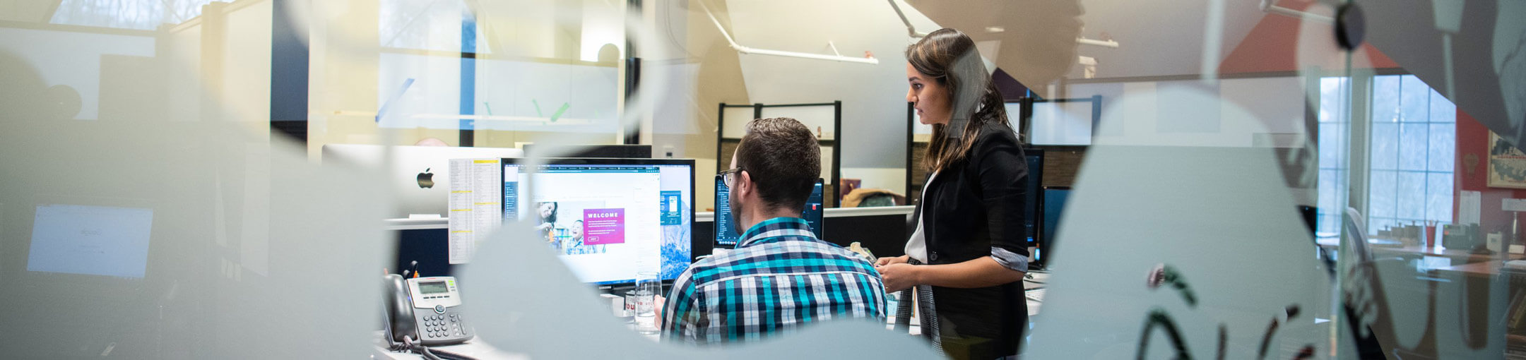 A pair of co-workers in an office looking at a webpage on a monitor.