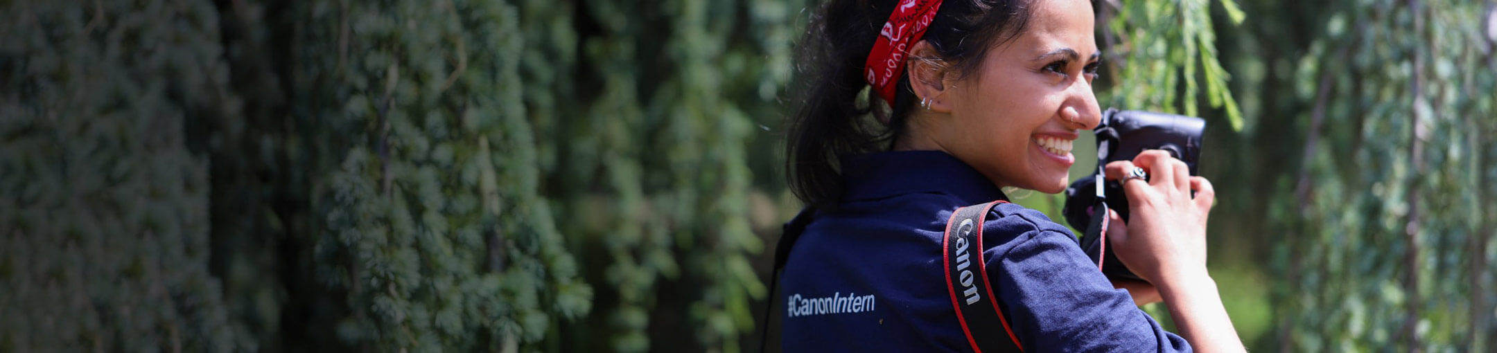 An RIT student holding a camera and wearing a shirt that reads Canon Intern.